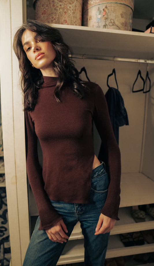 A woman wearing a dark brown turtleneck knit sweater with a side slit, paired with blue jeans. LUCE