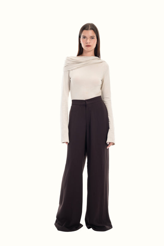 Woman wearing a beige sweater and dark pants on a white background