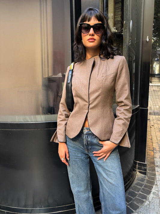 LUCE Woman wearing a beige blazer and blue jeans standing in front of a glass door in milan
