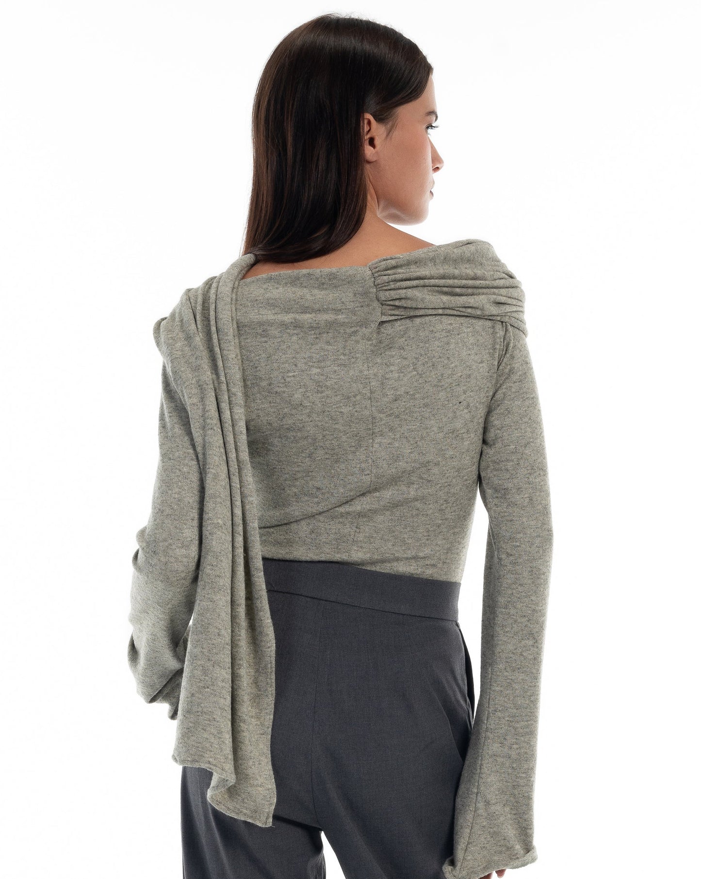 LUCE Woman wearing a gray sweater with acape scarf, standing against a white background