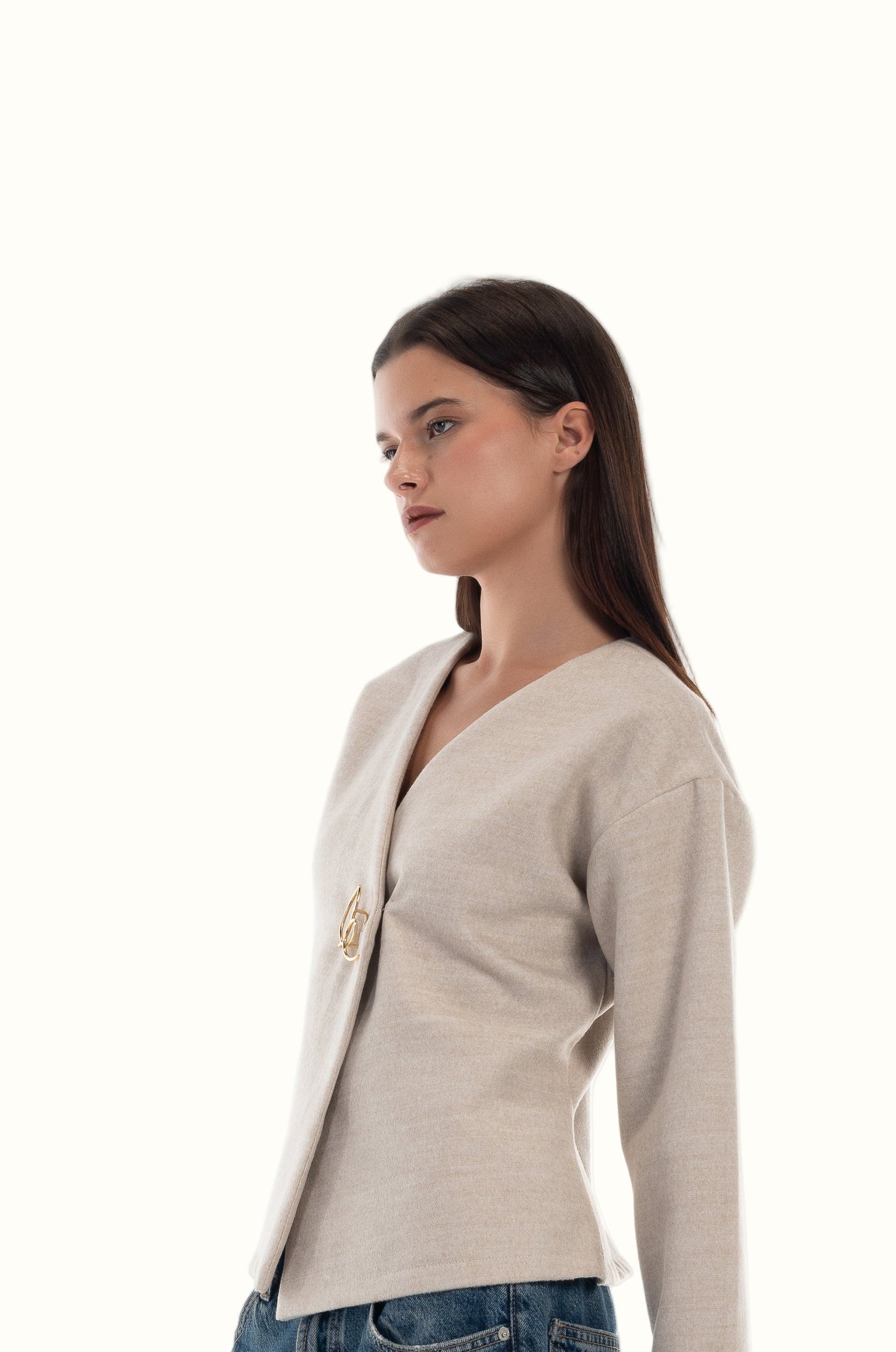 Woman wearing a beige cardigan with LUCE signature logo brooch on a white background