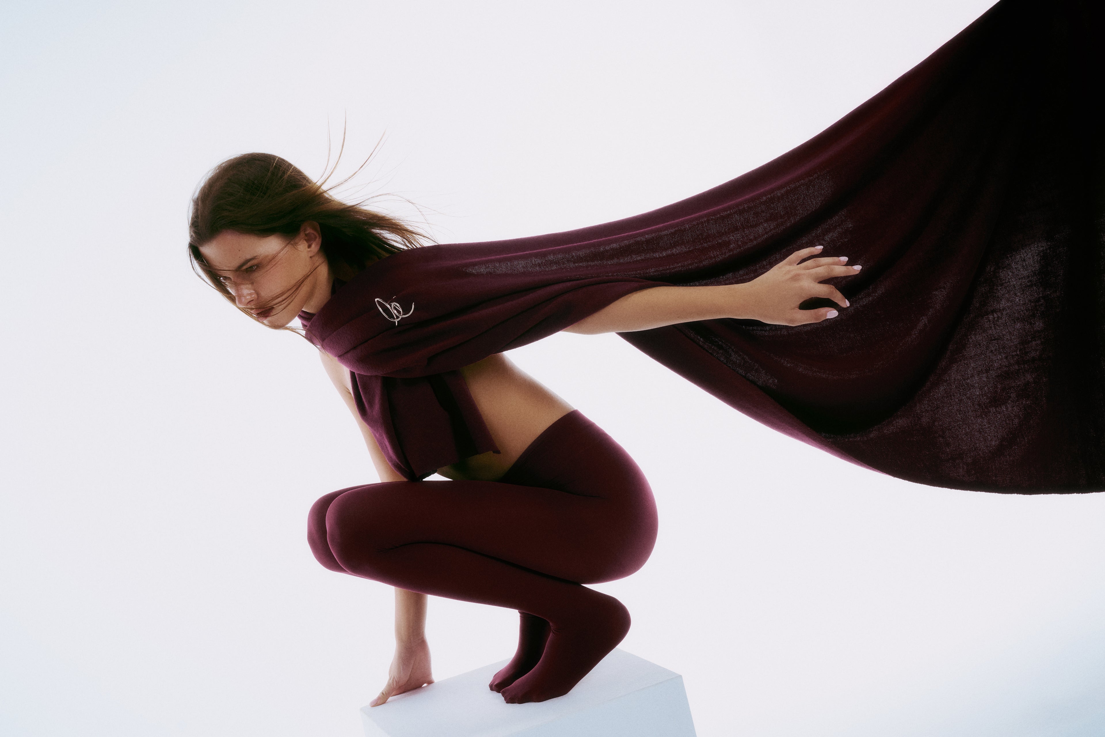 LUCE Woman in burgundy outfit with flowing scarf with a gold brooch against a light background