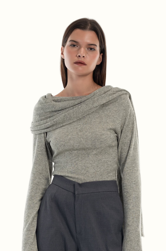 Woman wearing a gray long-sleeve knit top with attached scarf and dark gray pants on a white background